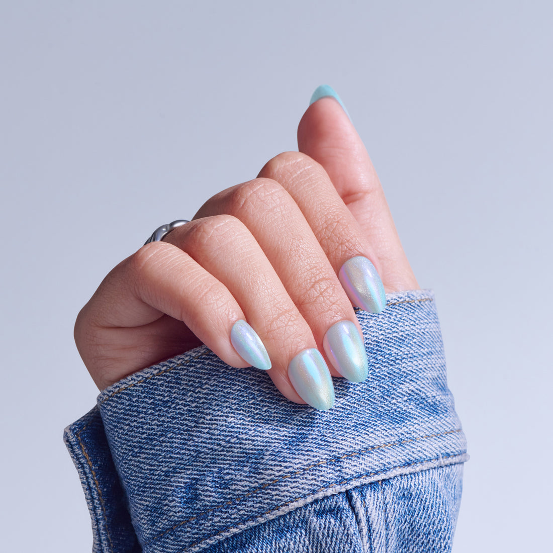 Hand with iridescent nail polish and light blue nail tips, wearing denim sleeve.