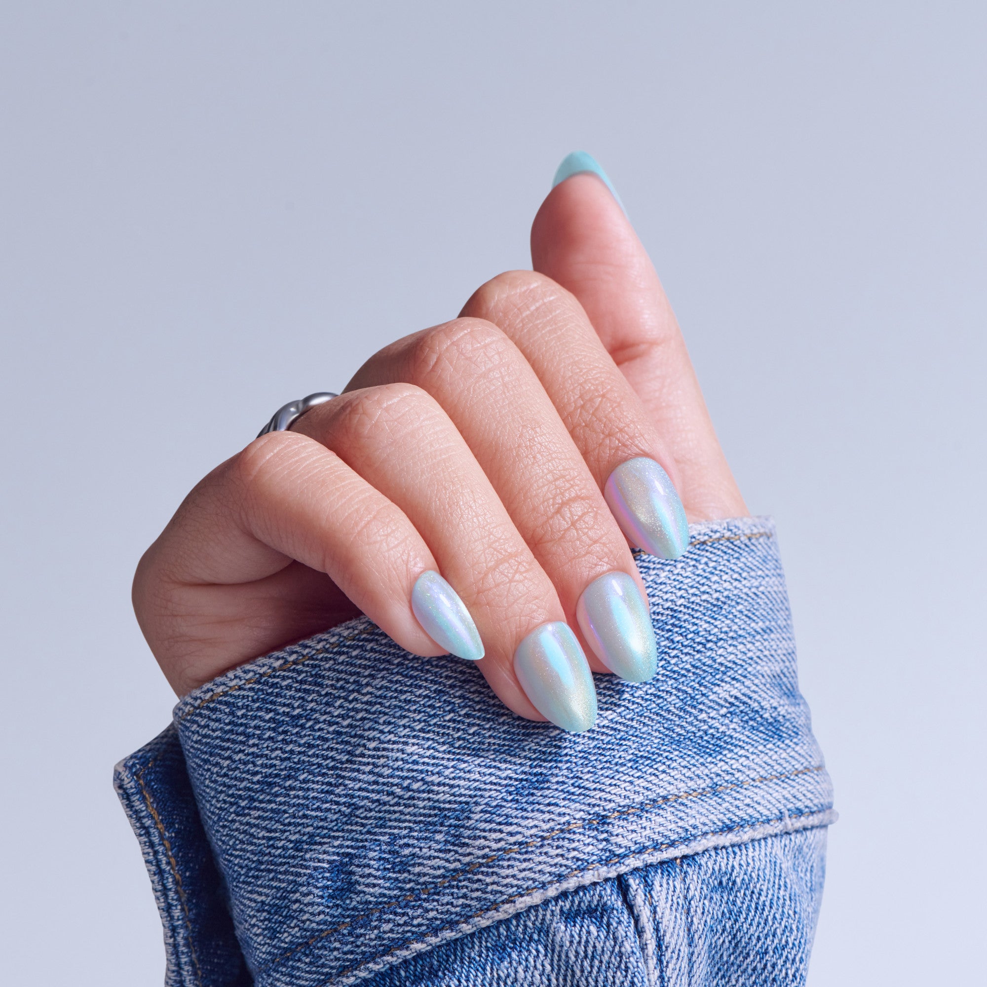 Hand with iridescent nail polish and light blue nail tips, wearing denim sleeve.