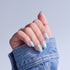 Hand with iridescent nail polish and light blue nail tips, wearing denim sleeve.