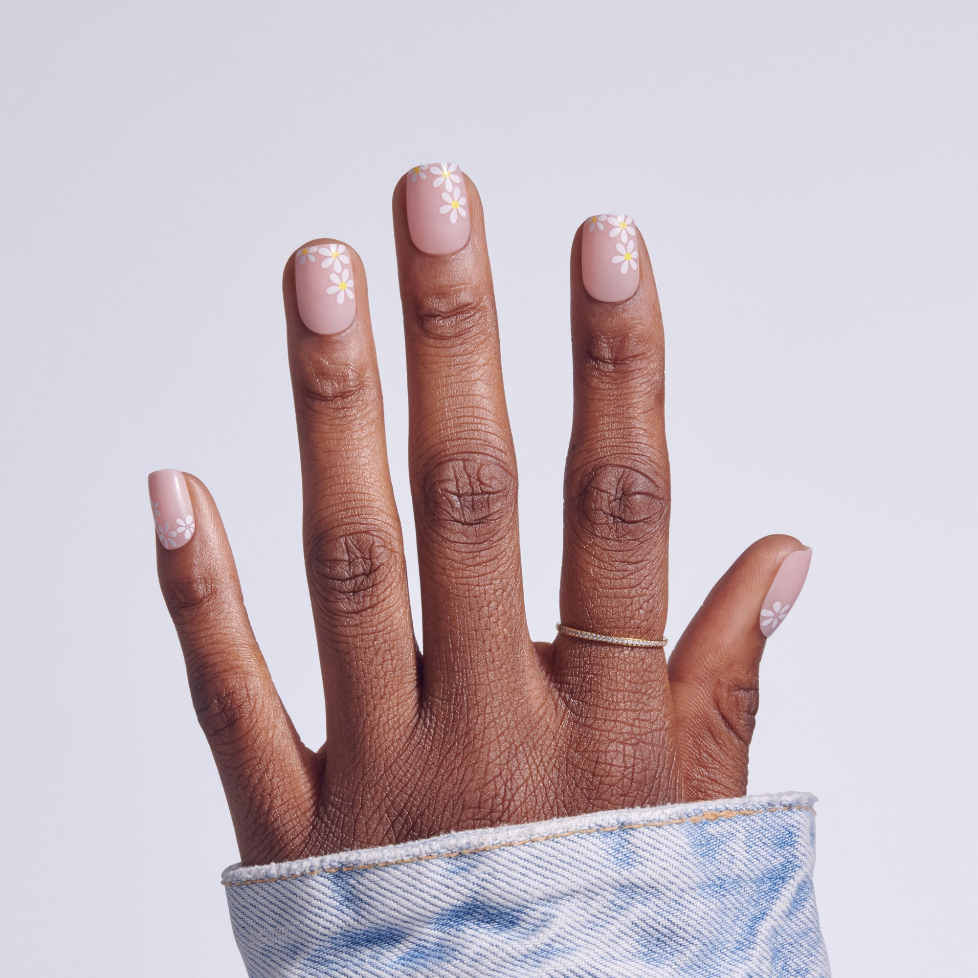 Hand with pink nails featuring white daisy flower designs, wearing blue patterned sleeve.