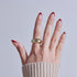 Hand with red French tip manicure and gold ring against gray background.