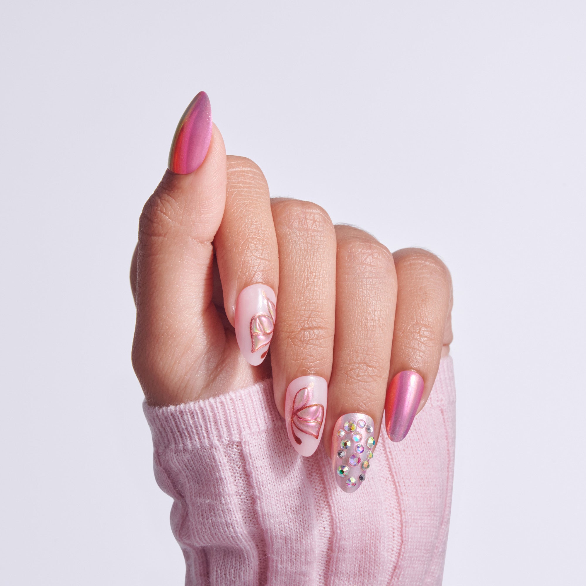 Hand displaying manicure with pink almond nails, leaf designs, and rhinestone accent nail.