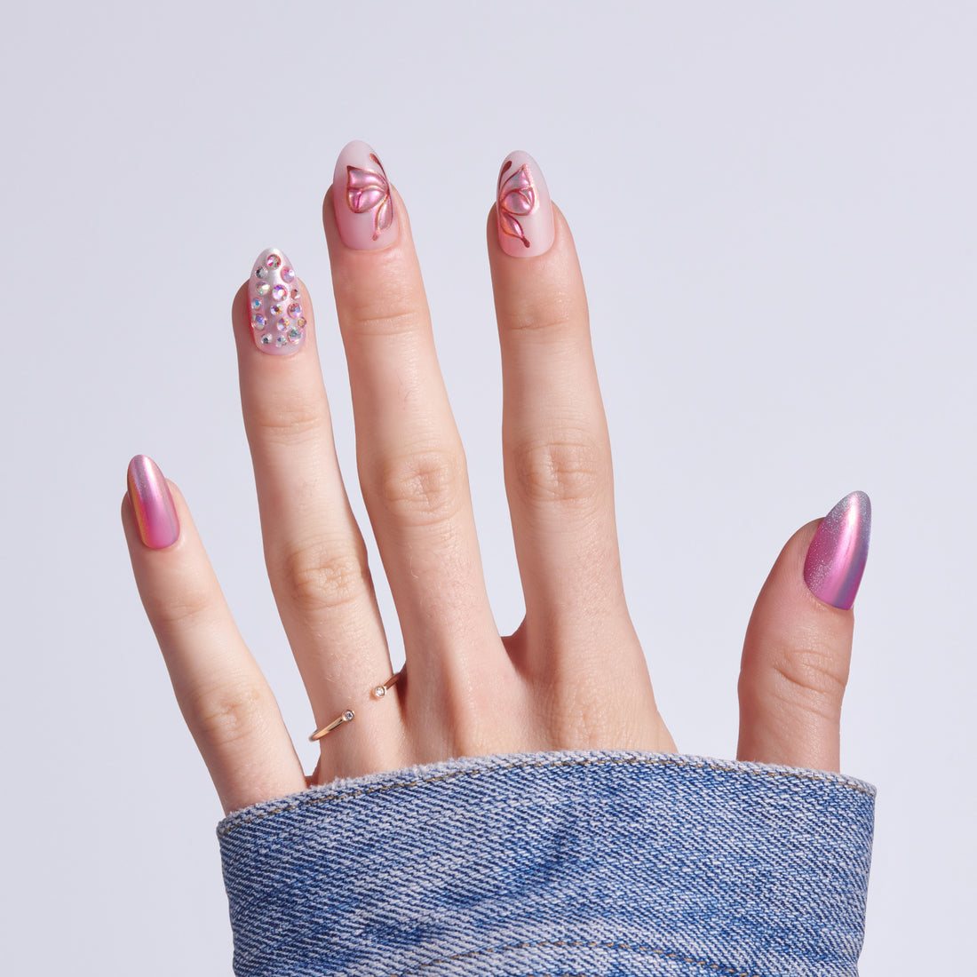 Hand displaying five different pink nail designs with sparkles and butterfly patterns.