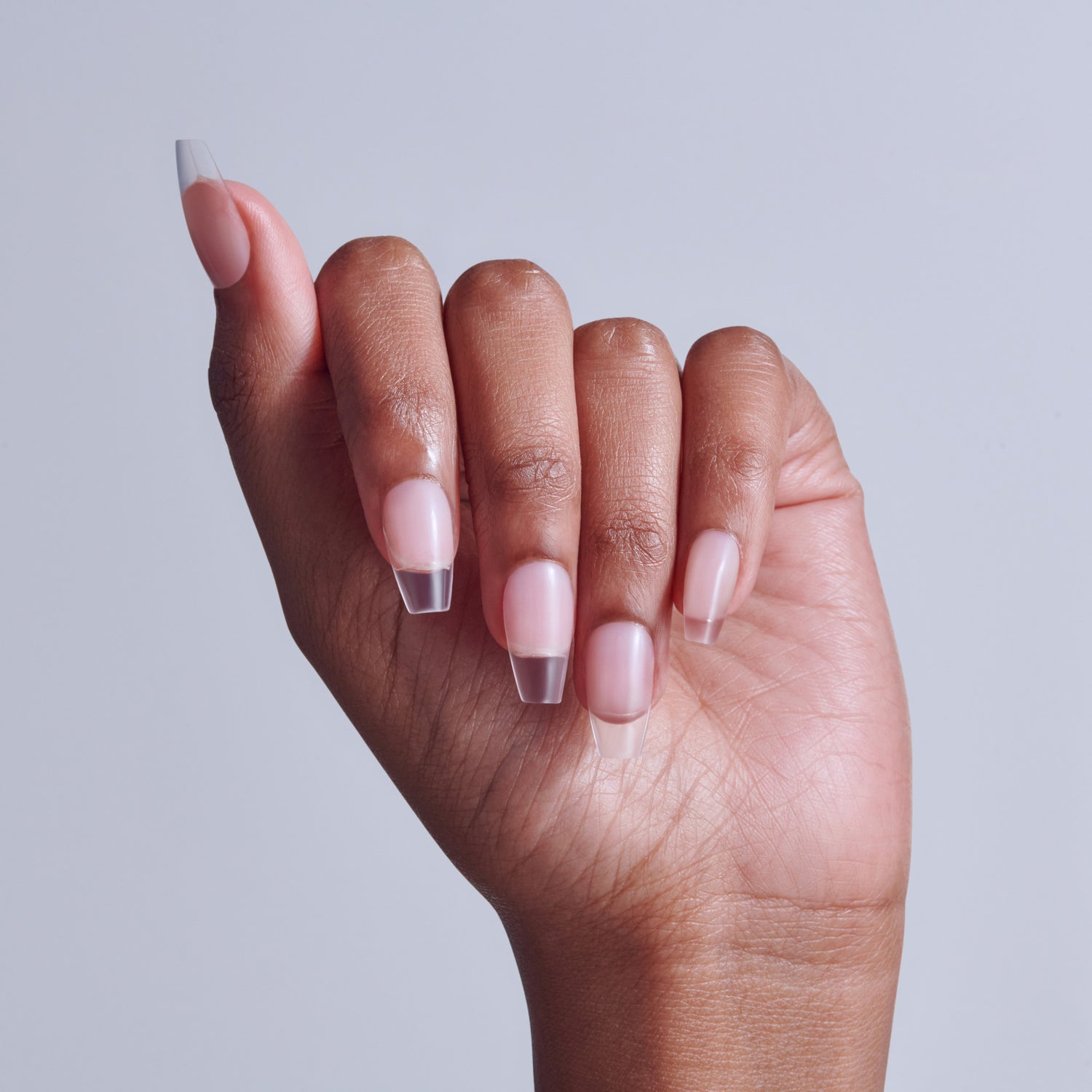Hand displaying pink and clear ombre coffin-shaped acrylic nails against light background.