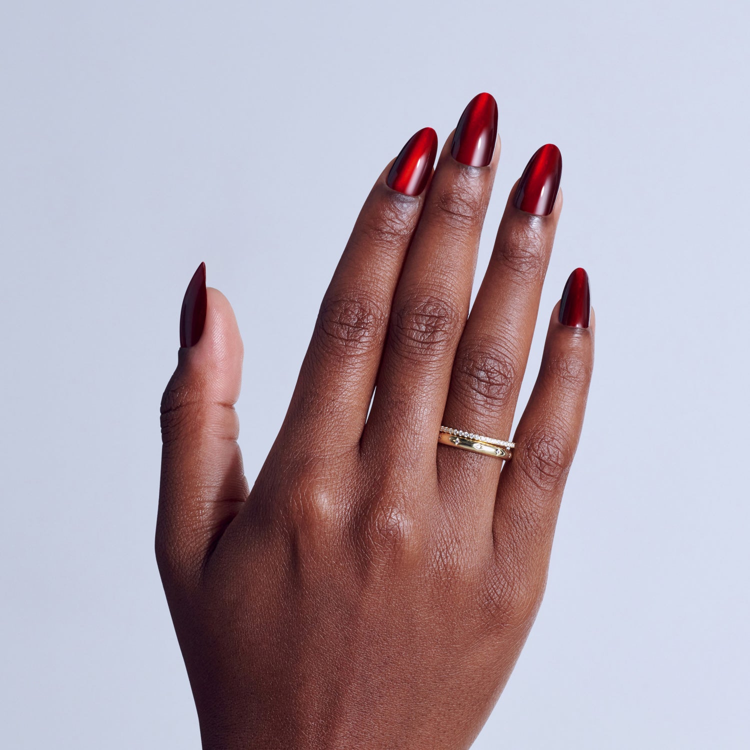 Hand with red metallic chrome nail polish and gold diamond ring on light blue background