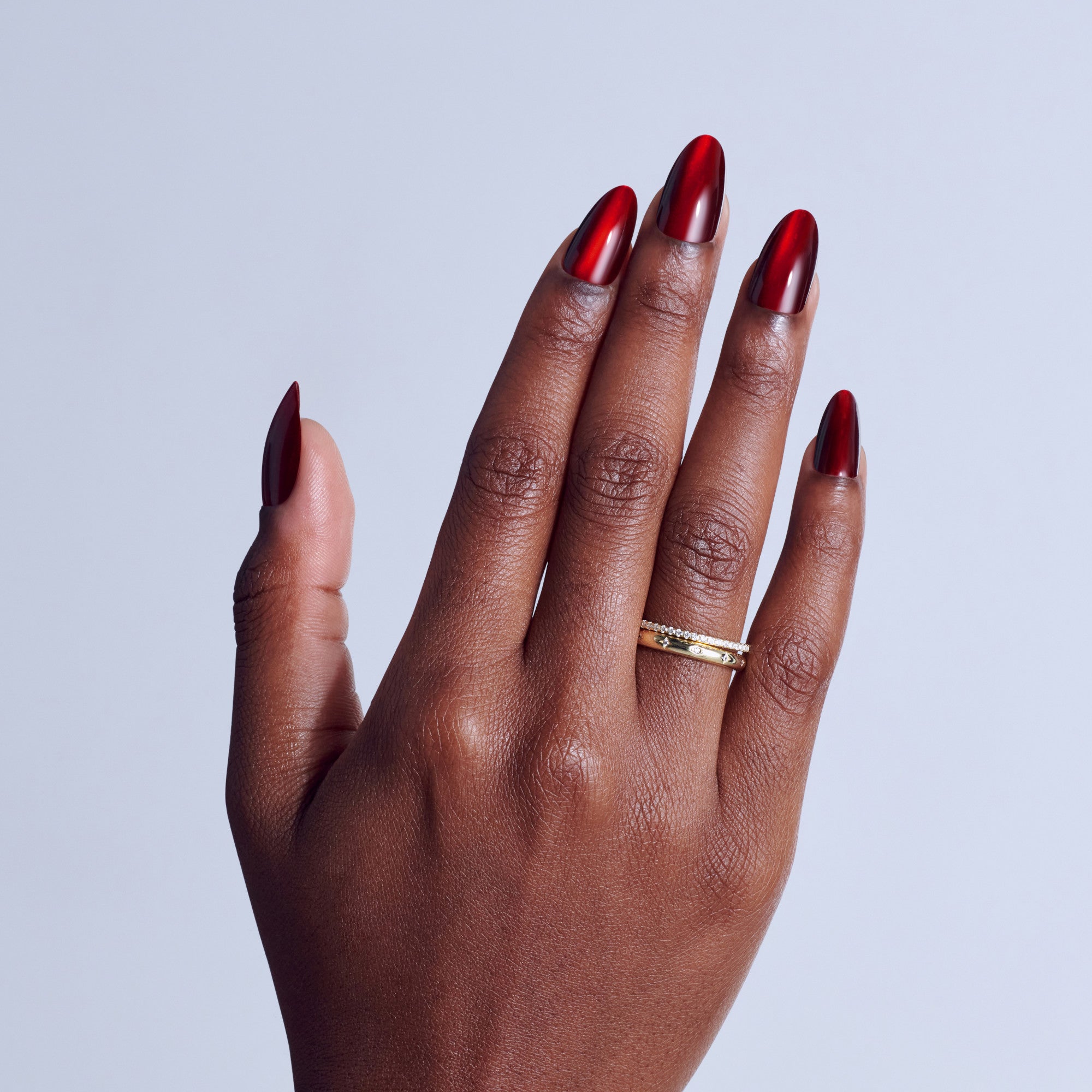 Hand with red metallic chrome nail polish and gold diamond ring on light blue background