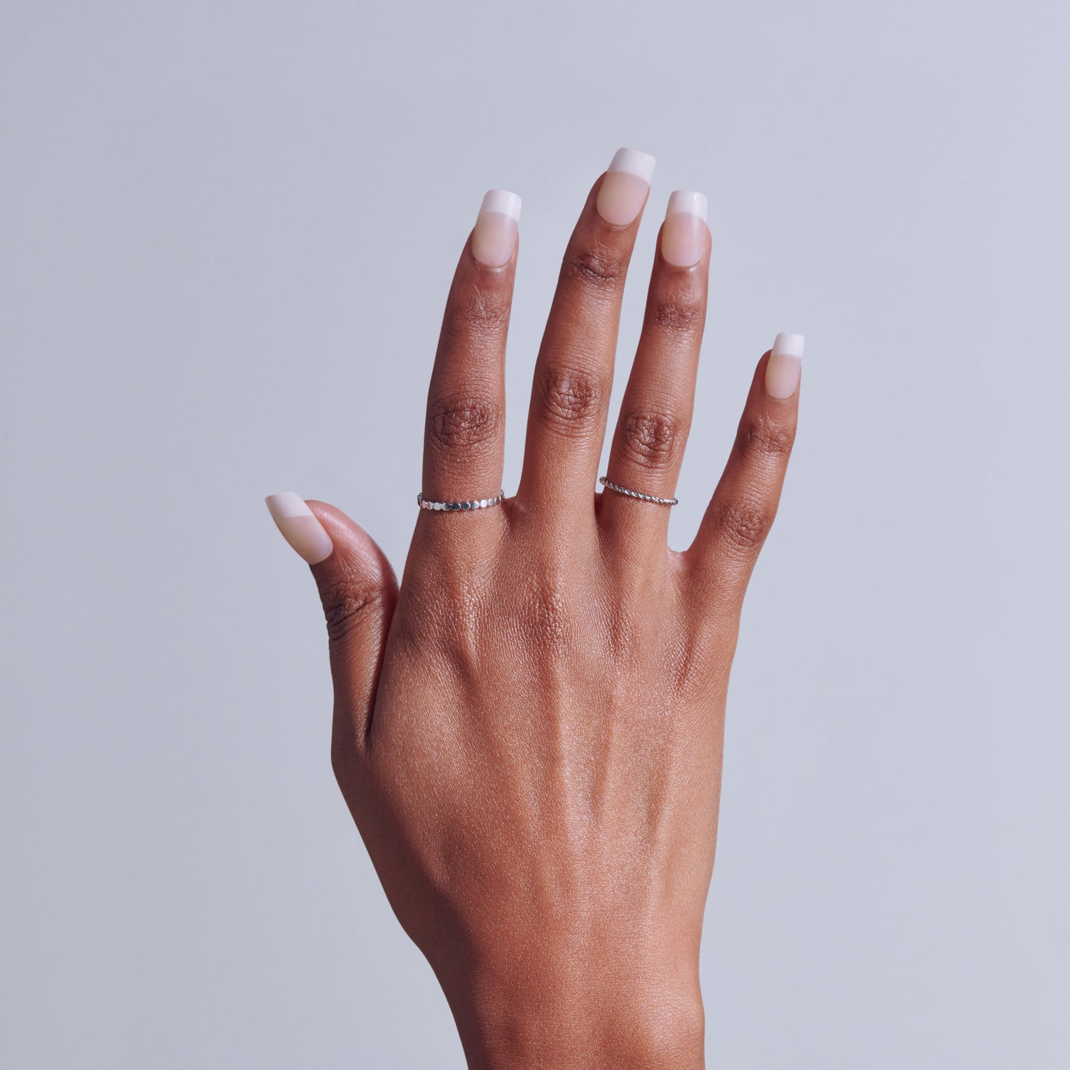 Hand with classic French manicure and diamond accent rings against gray background.