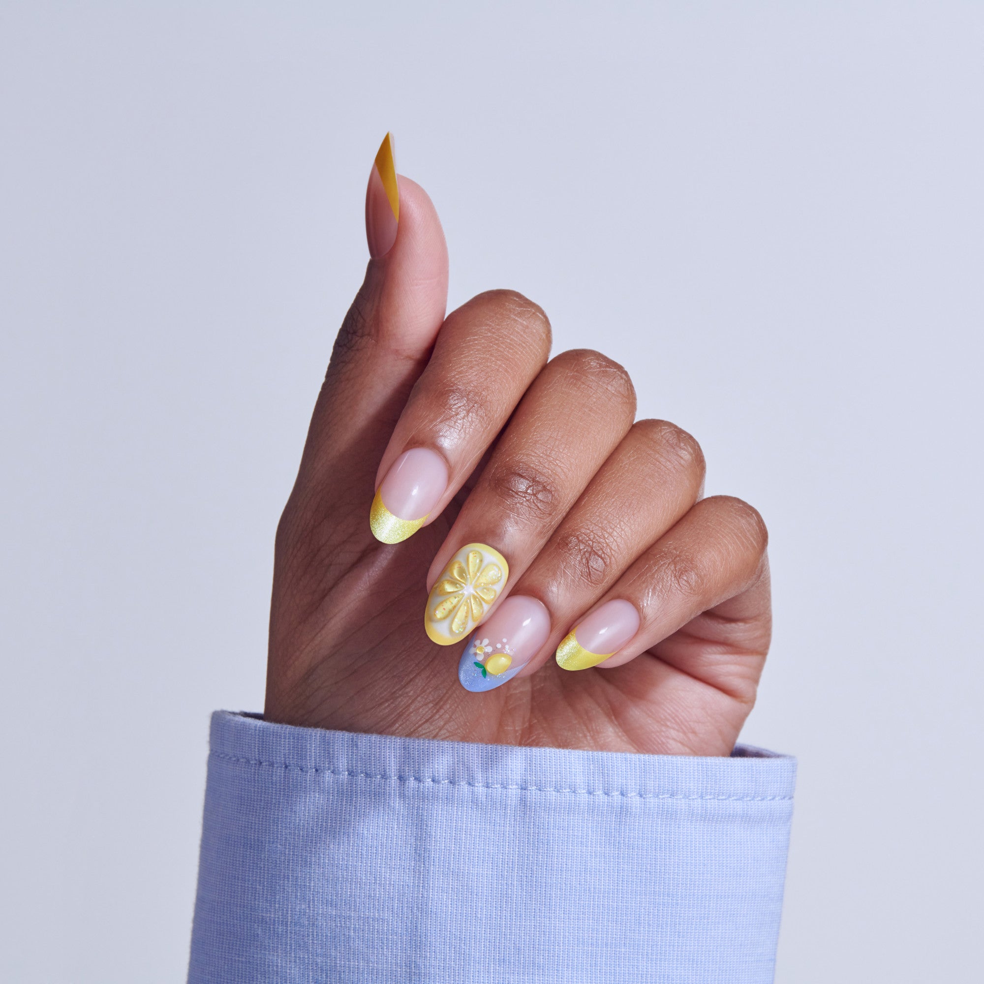 Hand displaying colorful nail art with yellow lemon slices, pink base, and blue accents on almond nails.
