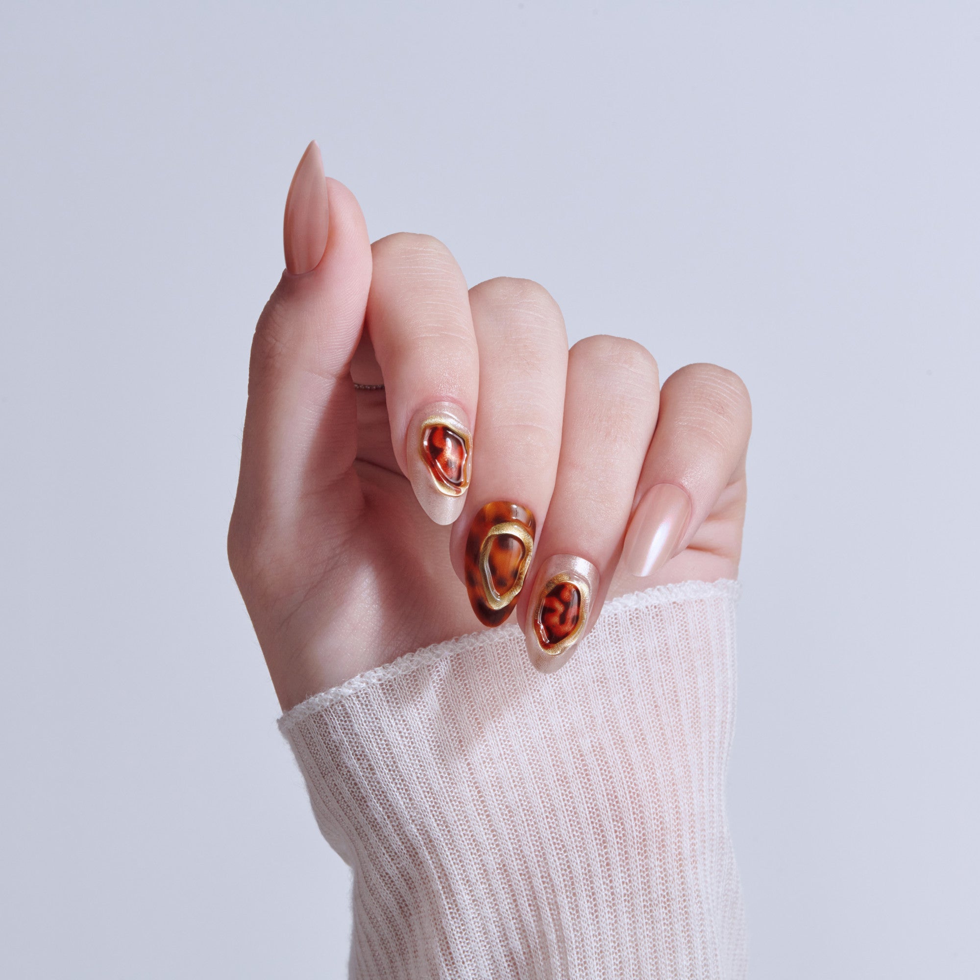 Hand displaying tortoiseshell nail art with gold accents on almond-shaped nails