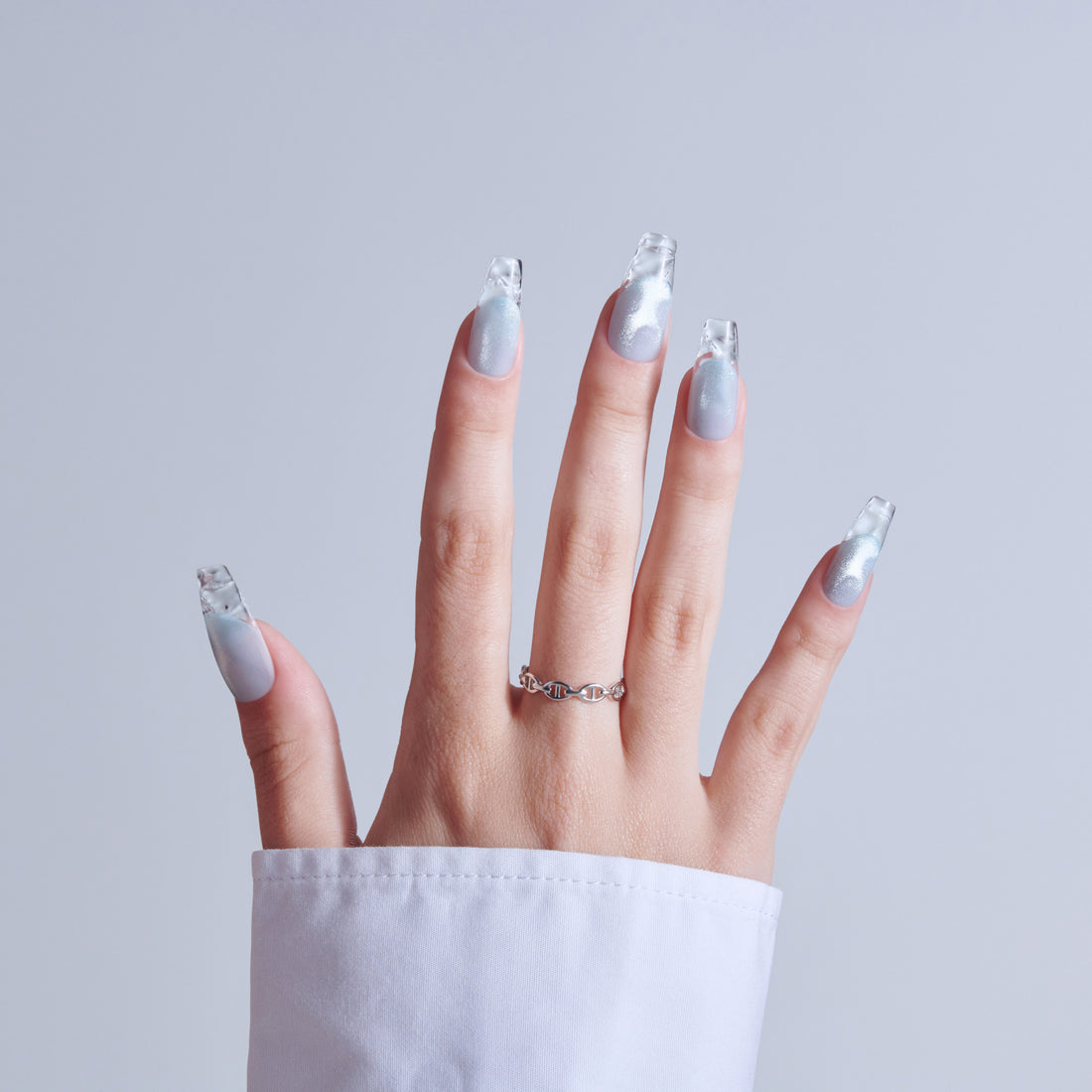 Hand with silver glitter acrylic nails and ornate silver ring against gray background.