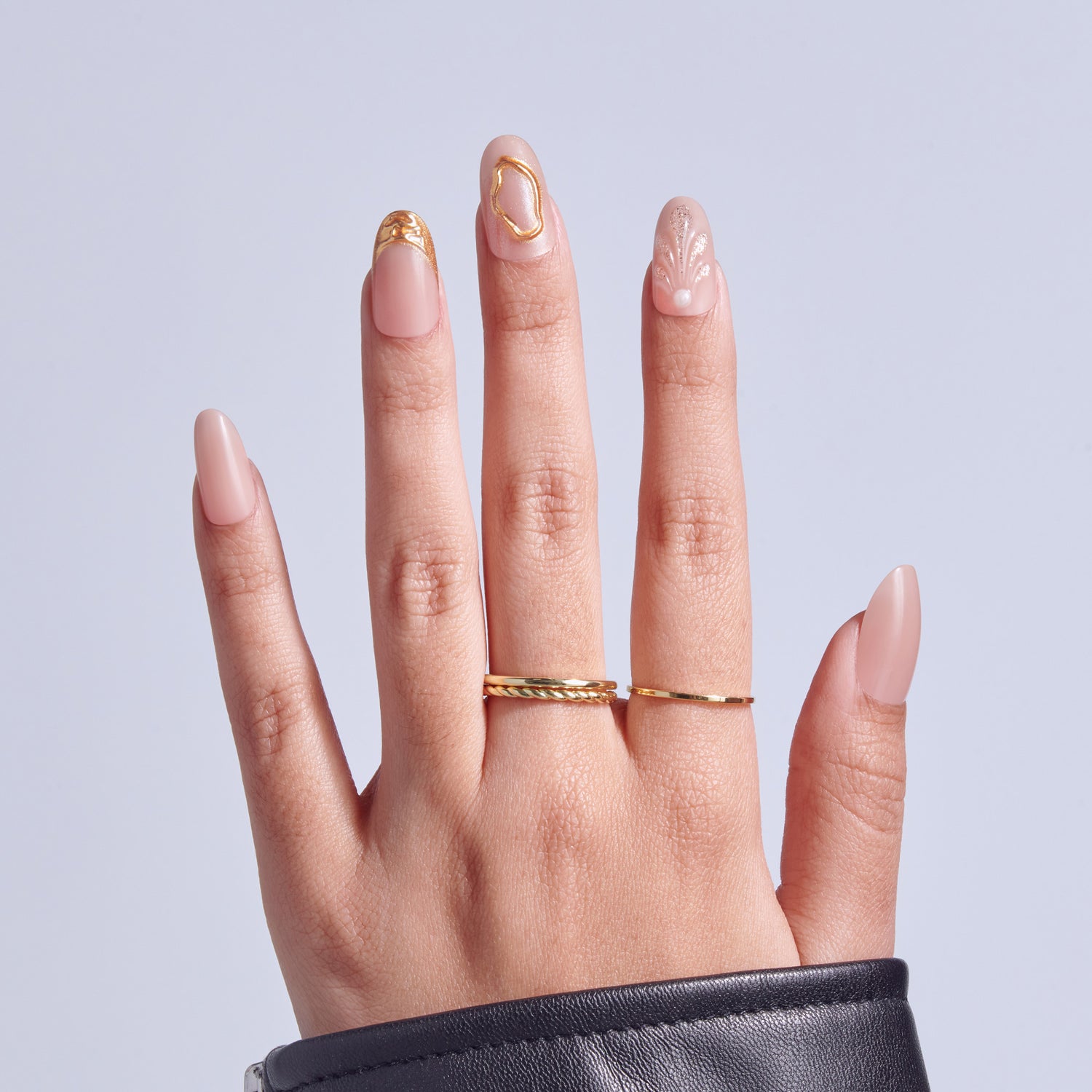 Hand displaying manicure with pink nails and gold accents, wearing twisted gold ring.