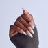 Close-up of manicured hand with white ombre almond nails and gold ring against light background.