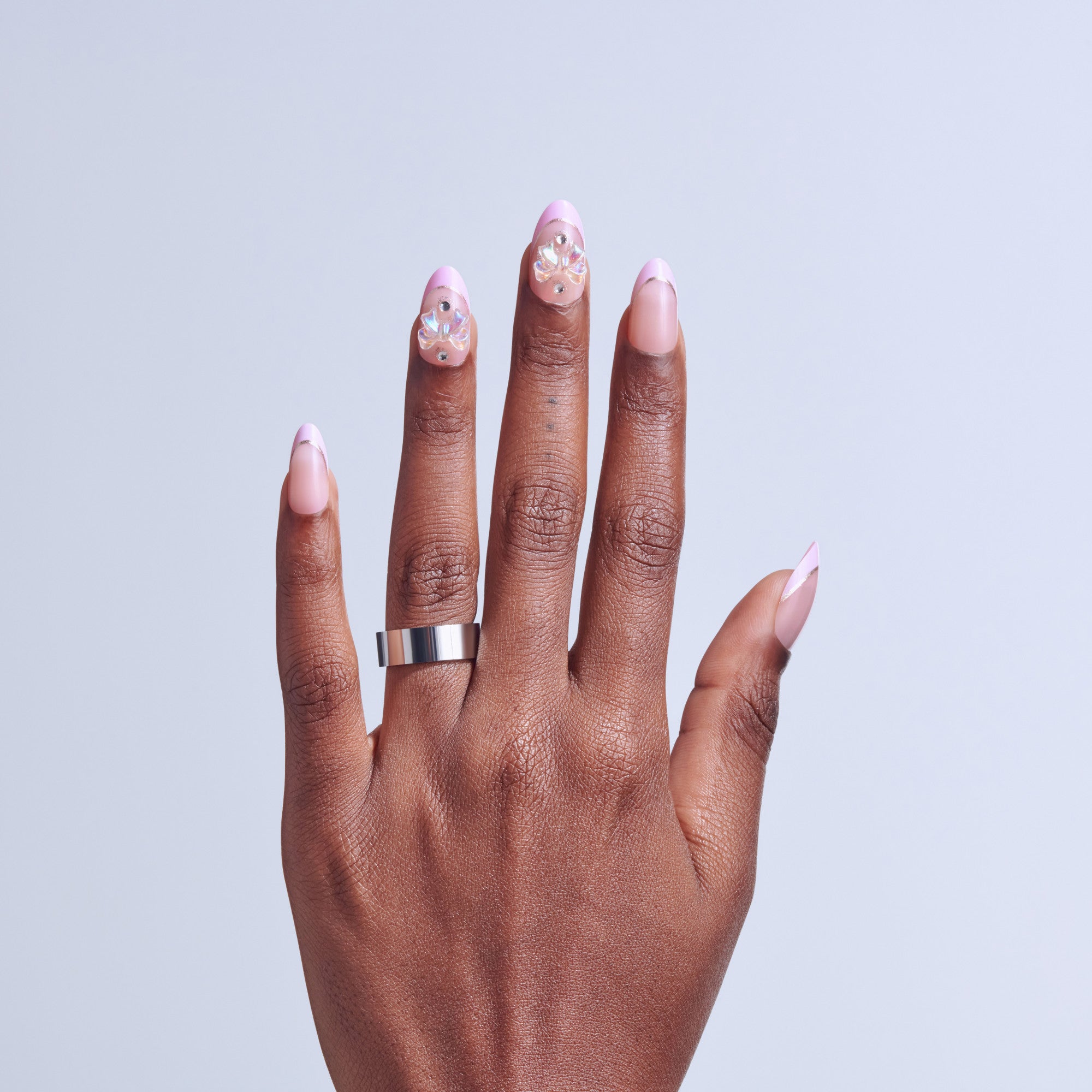 Hand displaying pink ombre nails with rhinestone embellishments and silver ring.
