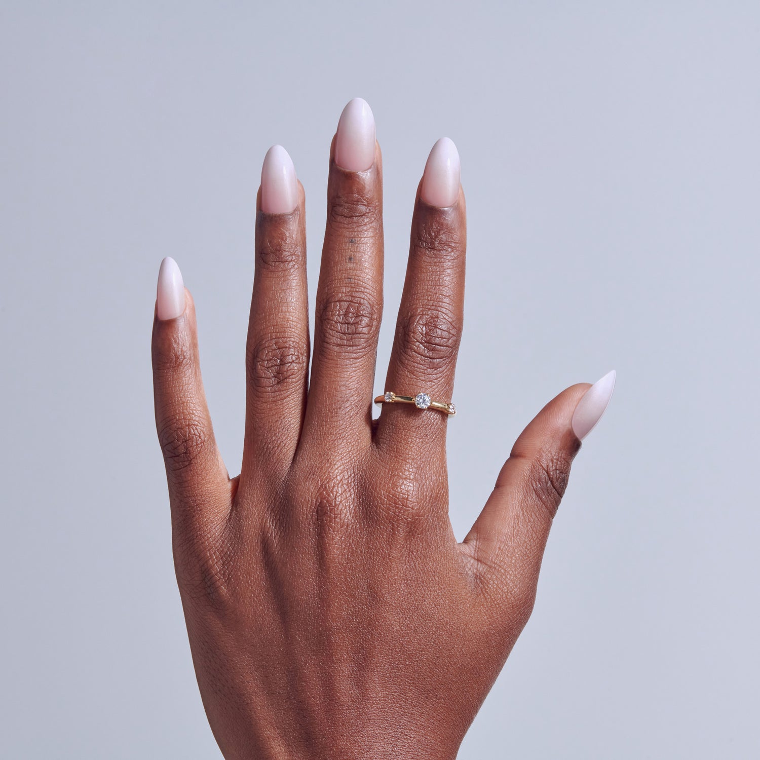 Hand with almond-shaped nails and engagement ring on light background