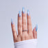 Hand displaying iridescent blue ombre gel nails with twisted metal ring against white background.