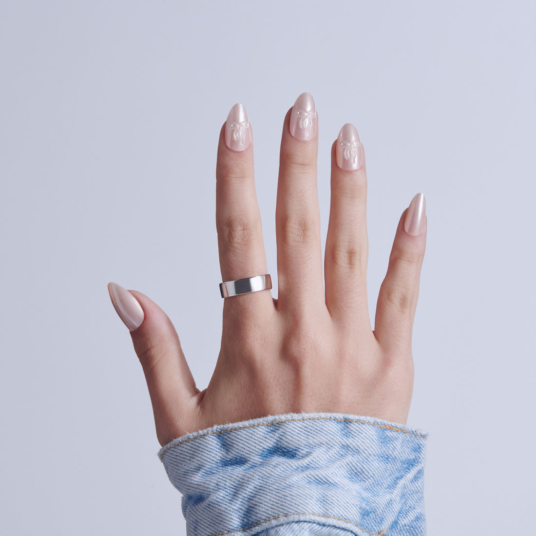 Hand displaying almond-shaped nails with white snowflake designs and pearl finish against light blue background.