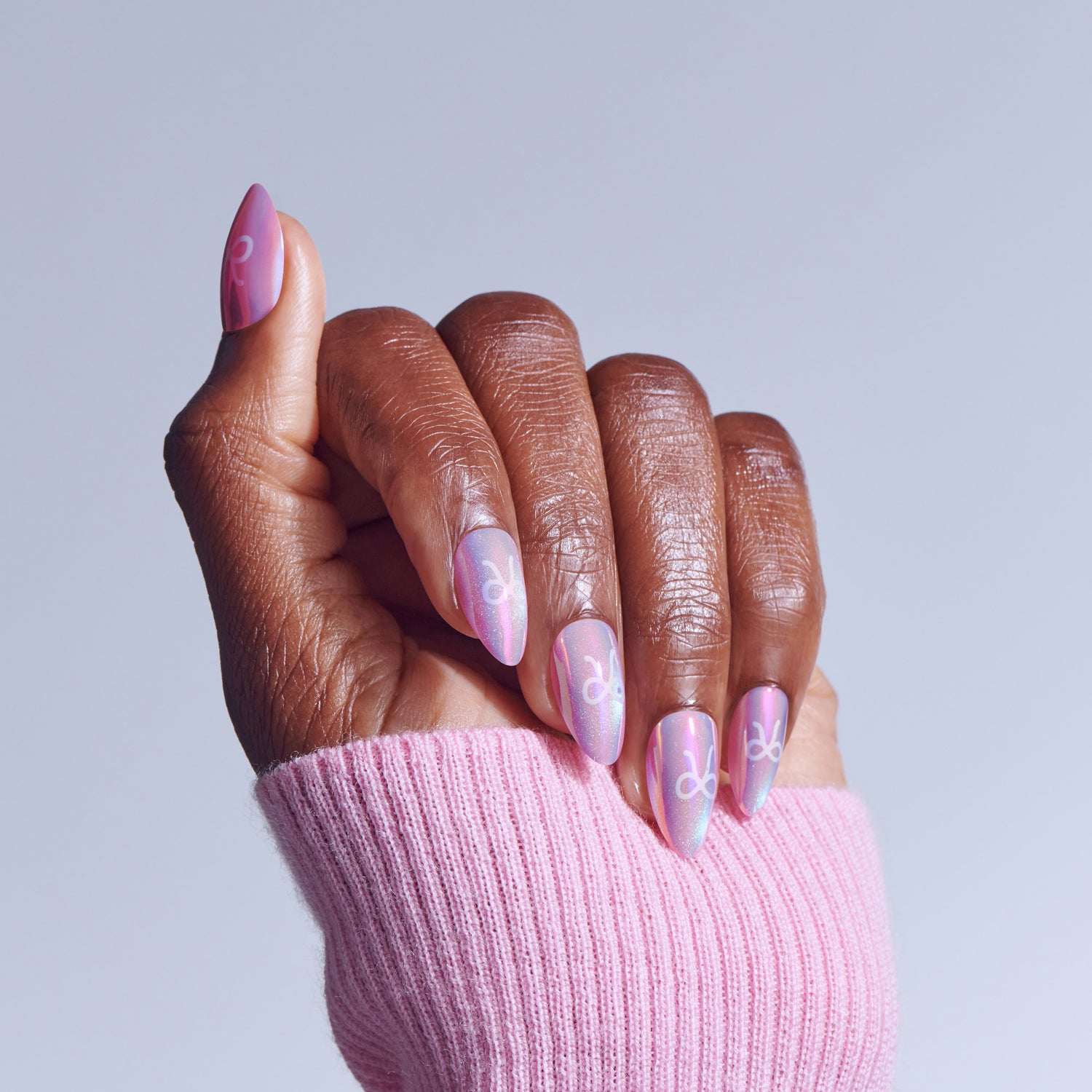 Hand with almond-shaped pink nails featuring zodiac symbol designs