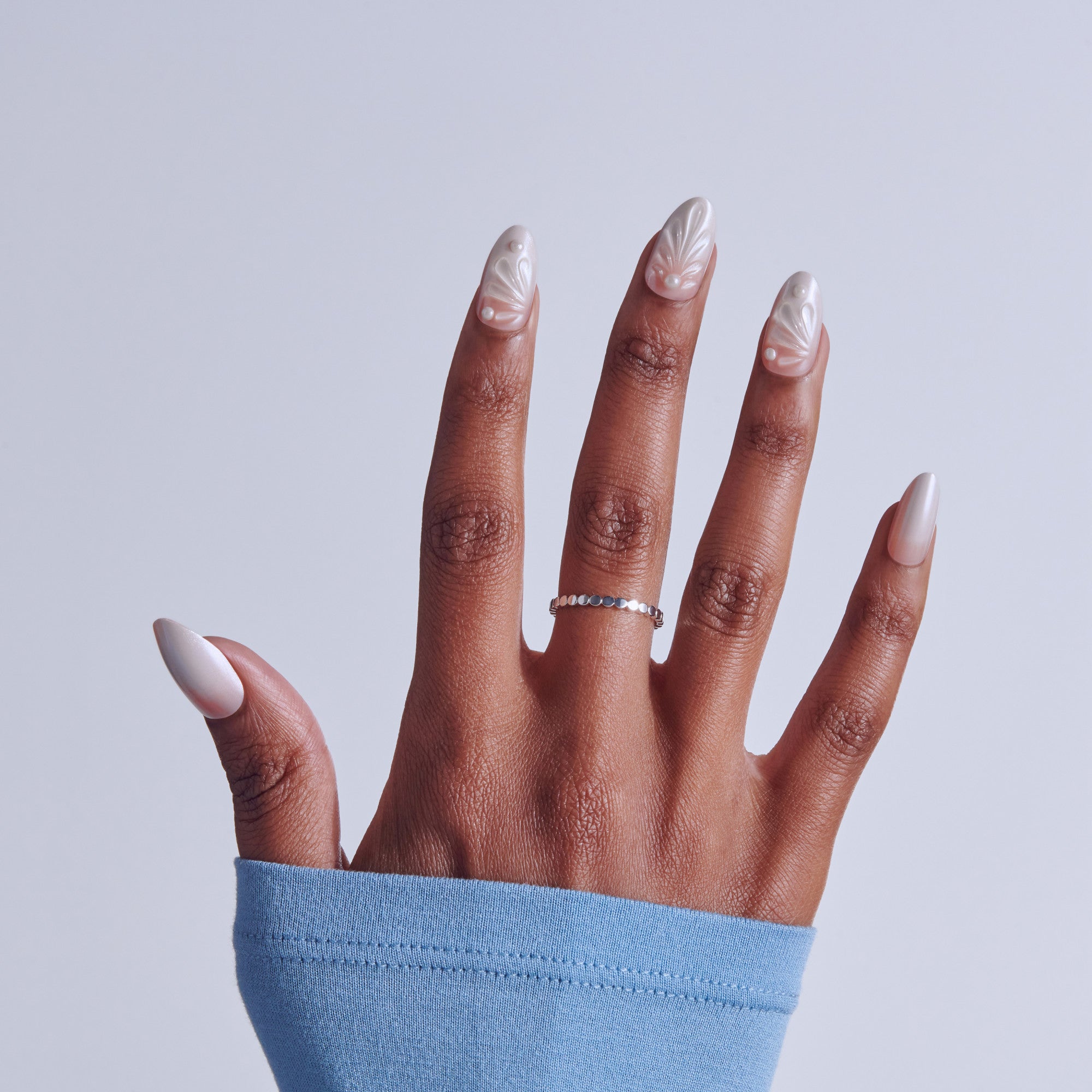 Hand displaying almond-shaped nails with white leaf nail art design and decorative ring.