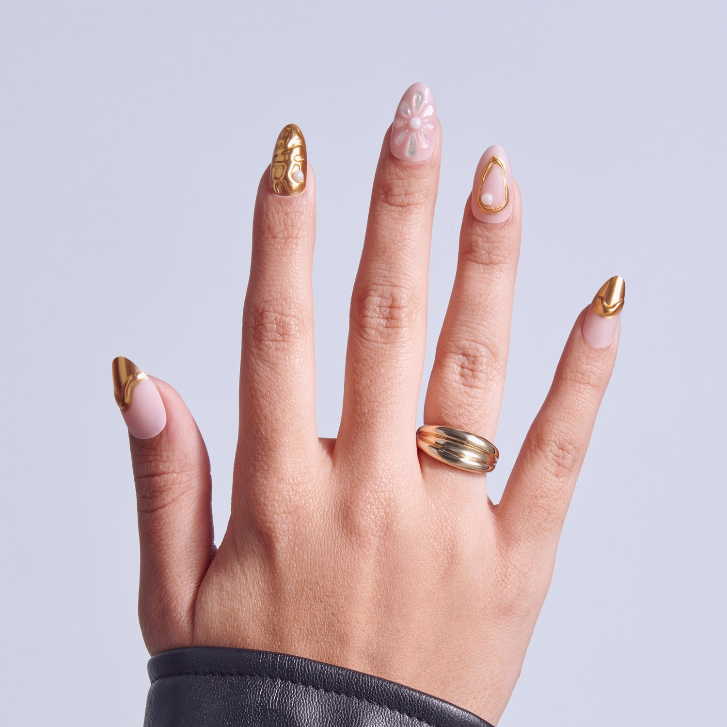 Hand displaying manicured nails with pink base and gold accents, wearing a gold ring.