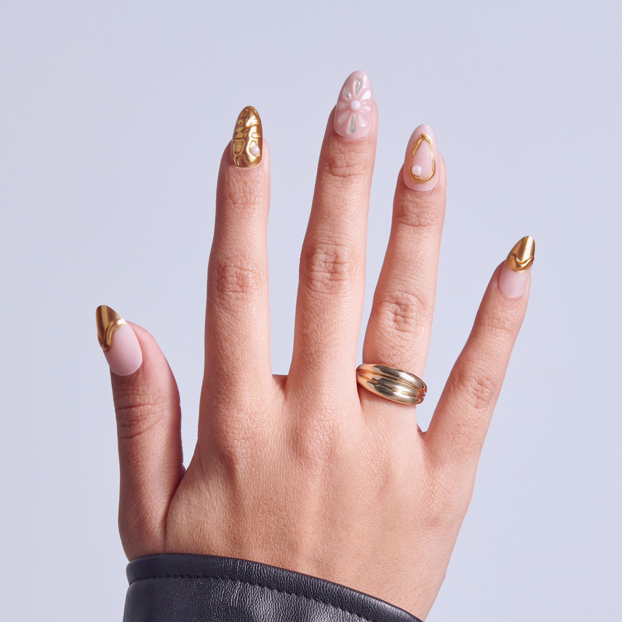 Hand displaying manicured nails with pink base and gold accents, wearing a gold ring.