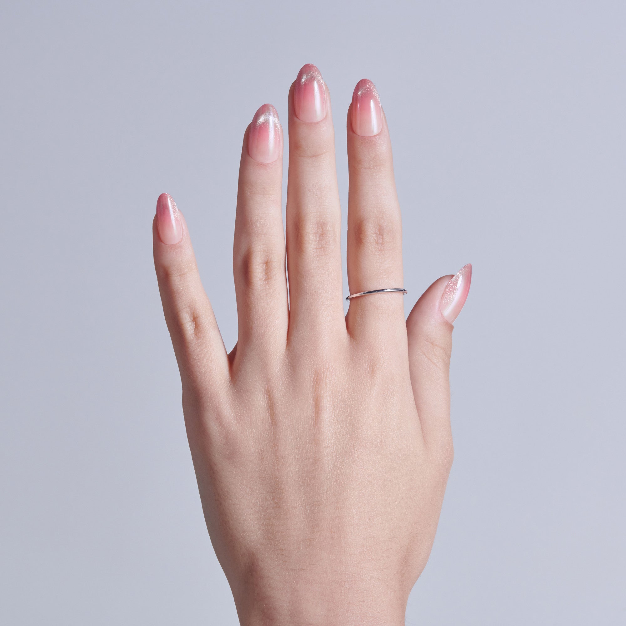 Hand with pink ombré acrylic nails and silver ring against gray background.