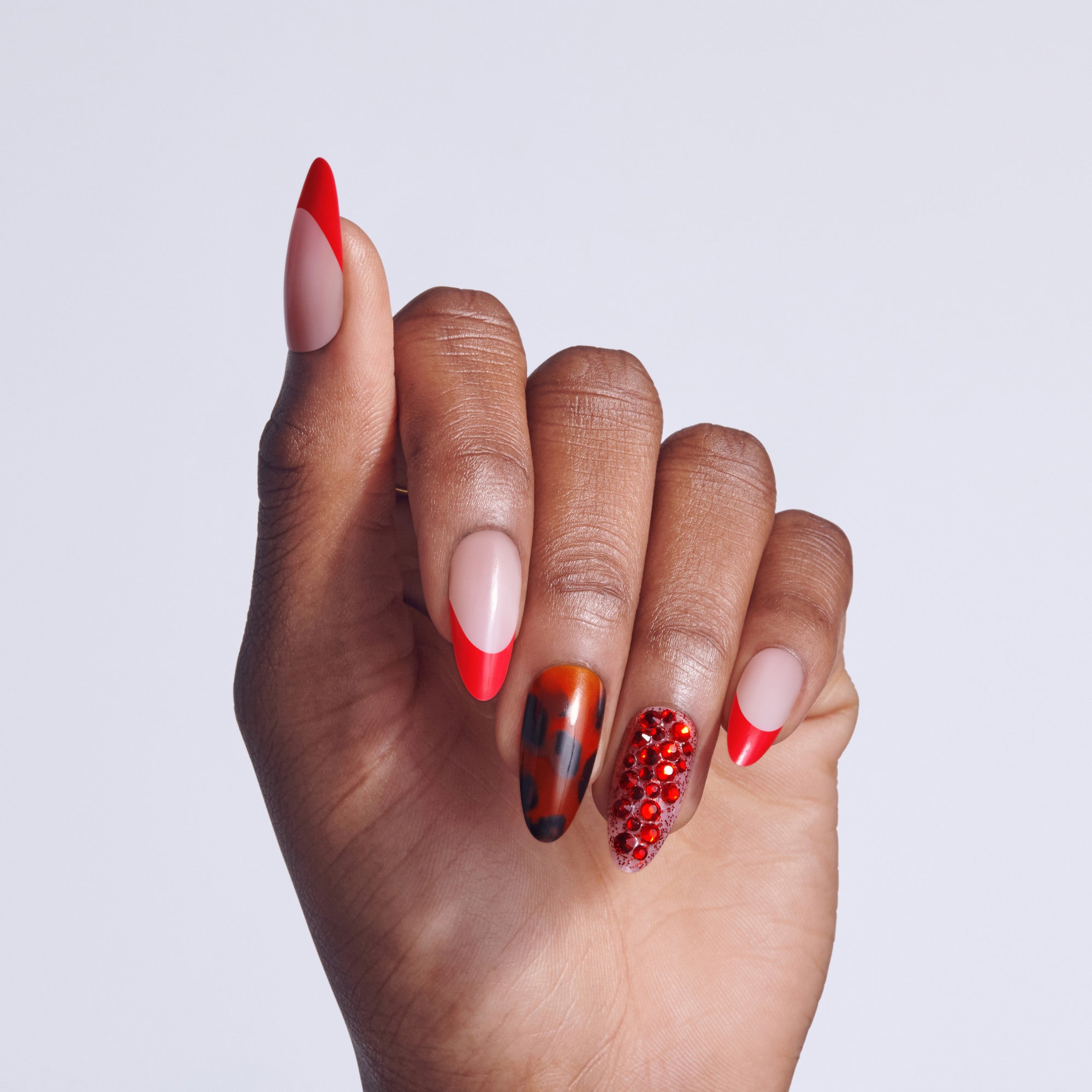 Hand displaying five red nail designs: almond shape, ombre, metallic, rhinestone accent, and French tip styles.