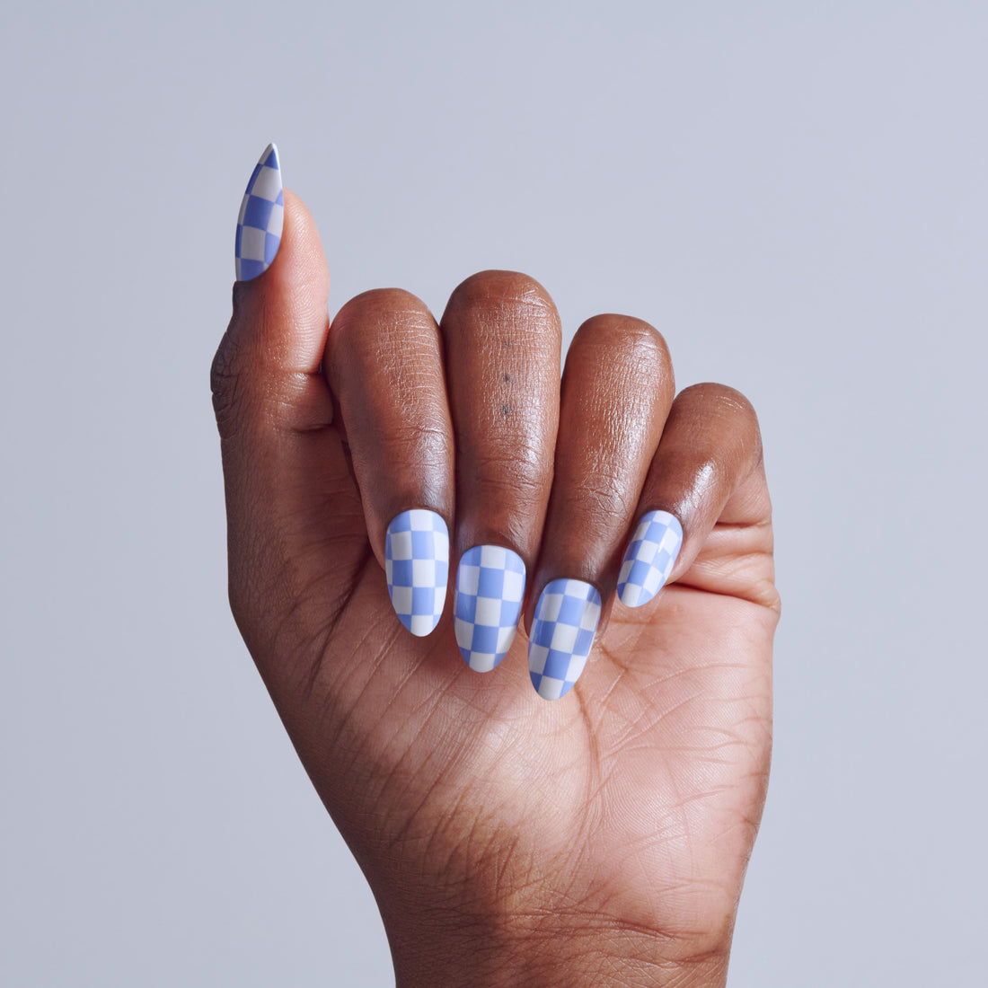 Hand displaying blue and white checkered nail polish on almond-shaped nails against gray background.