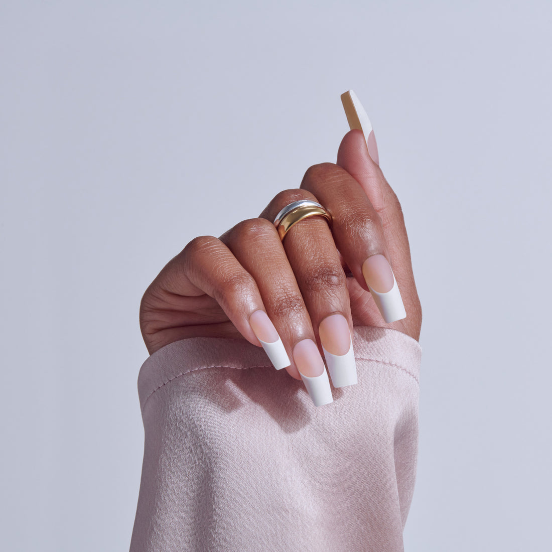 Hand displaying square acrylic nails with white tips and nude base, wearing gold ring.