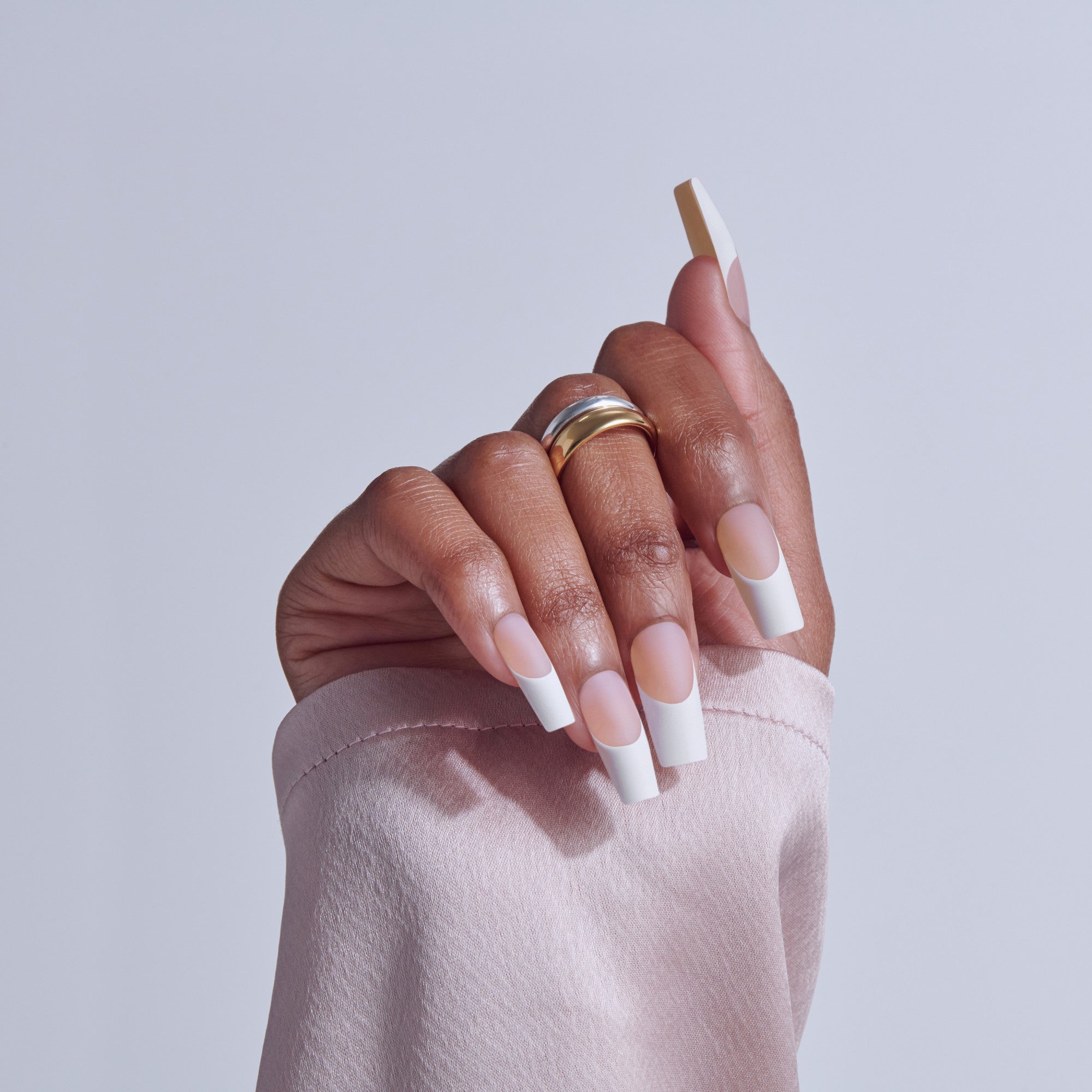 Hand displaying square acrylic nails with white tips and nude base, wearing gold ring.