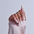 Hand displaying square acrylic nails with white tips and nude base, wearing gold ring.