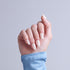 Hand with white almond-shaped manicure and blue sleeve against gray background