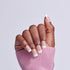 Hand with white-tipped French manicure nails in pink sweater against white background.