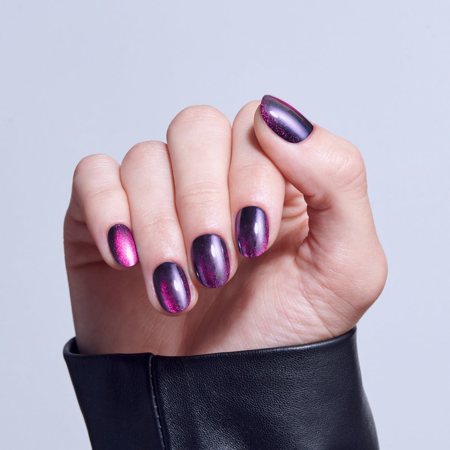 Purple and pink holographic nail polish on short nails, worn with black leather jacket.