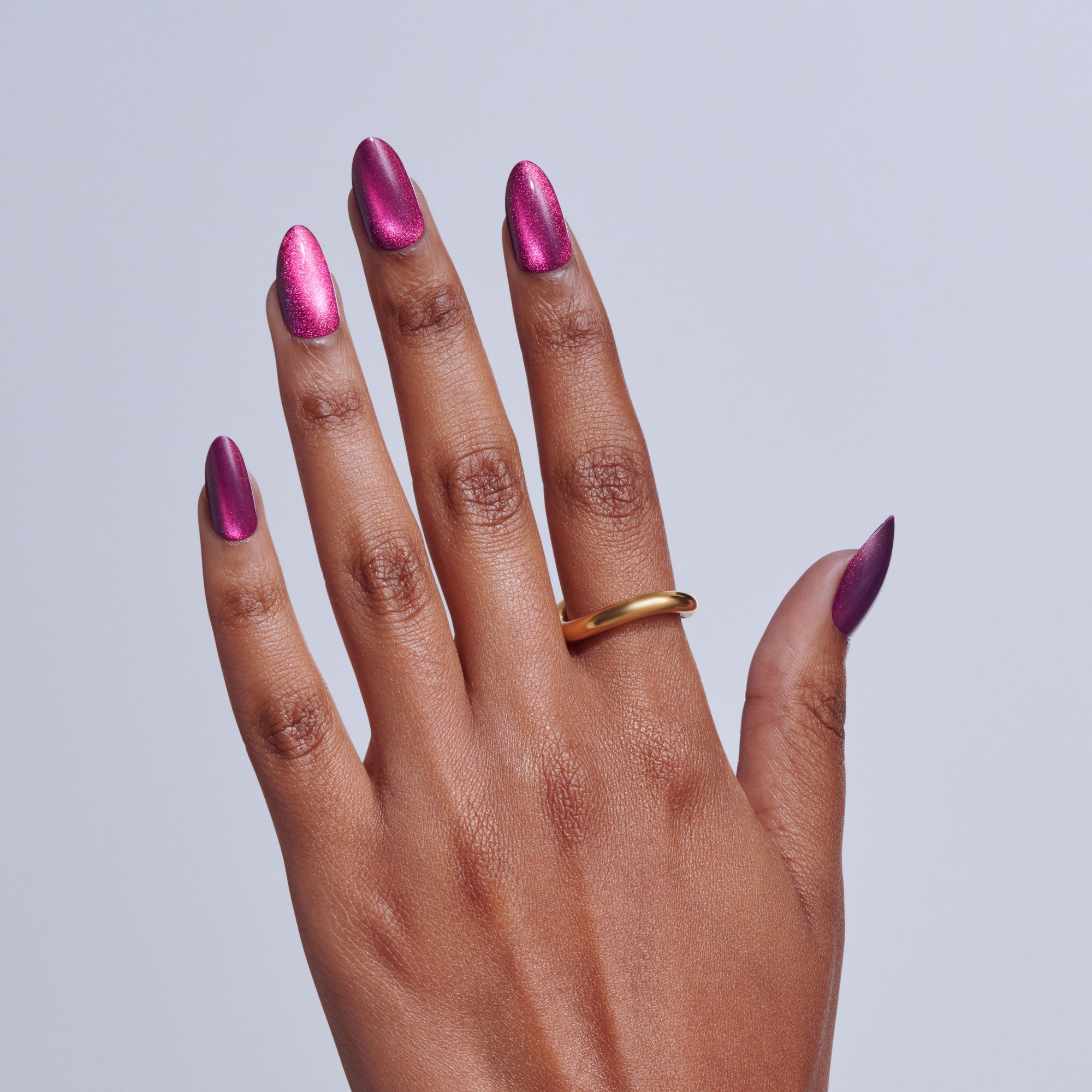 Hand with magenta metallic nail polish and gold ring on light background