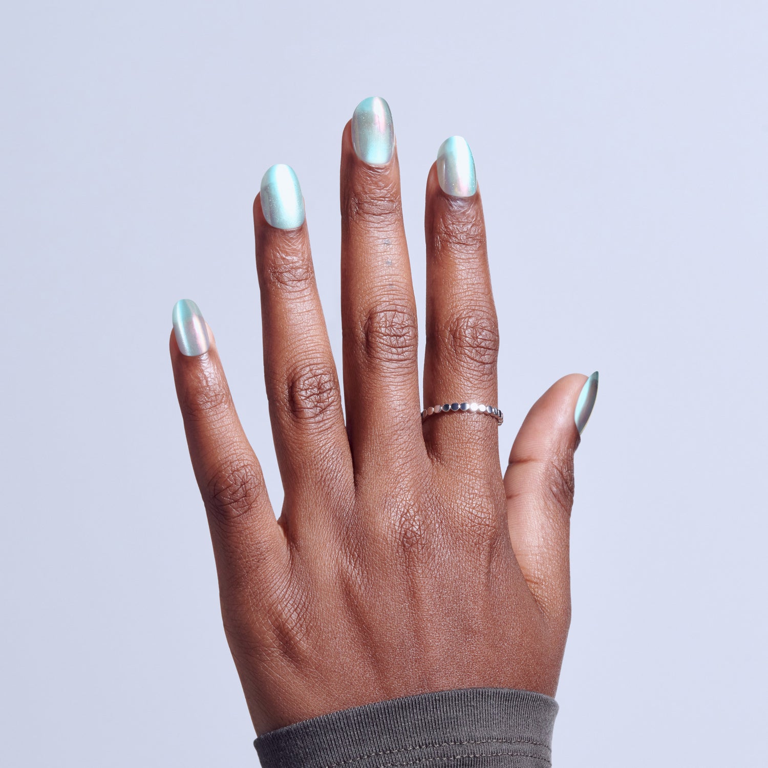 Hand with iridescent silver nail polish and delicate silver ring against white background.