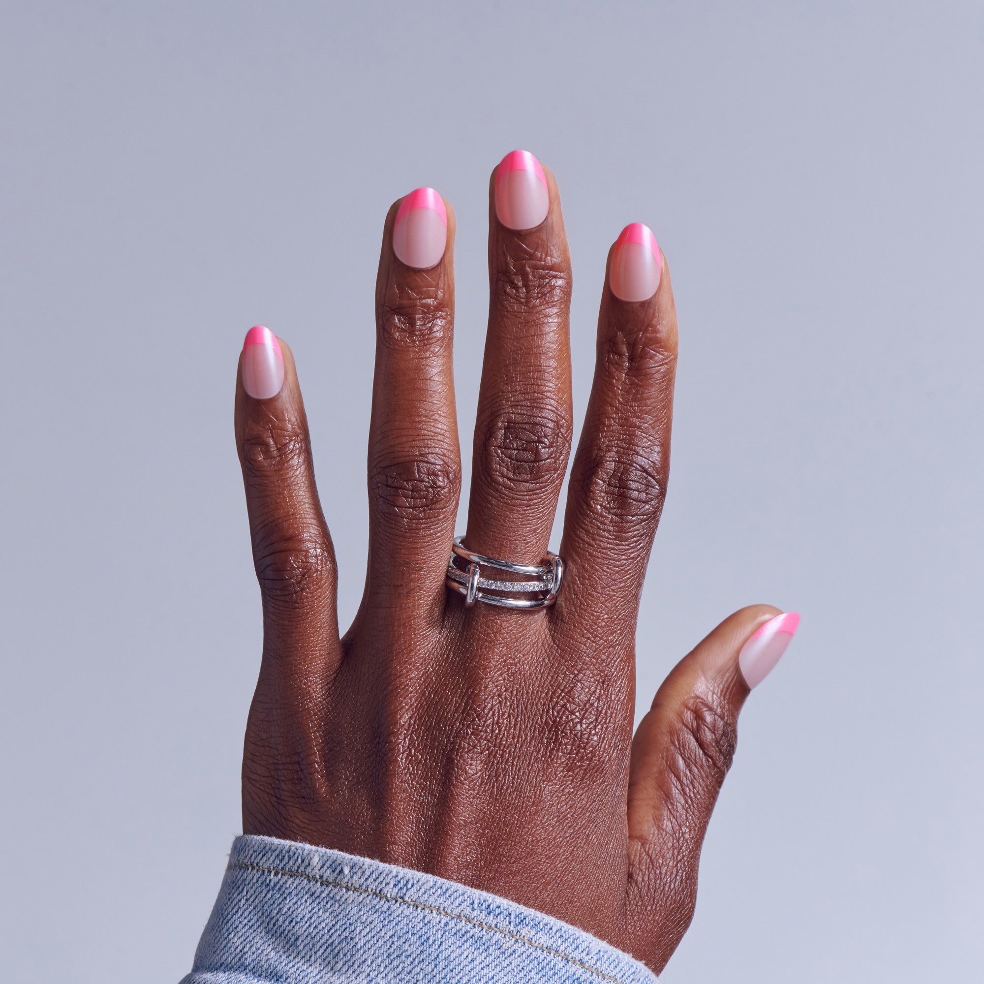 Hand with pink and white ombre nail polish and silver ring on gray background