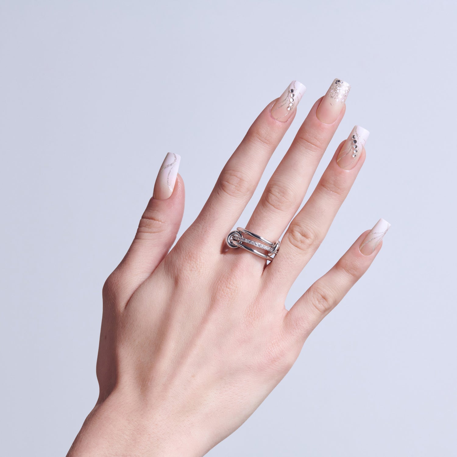 Hand wearing silver ring with diamond accents and pink glitter nail polish on light background.