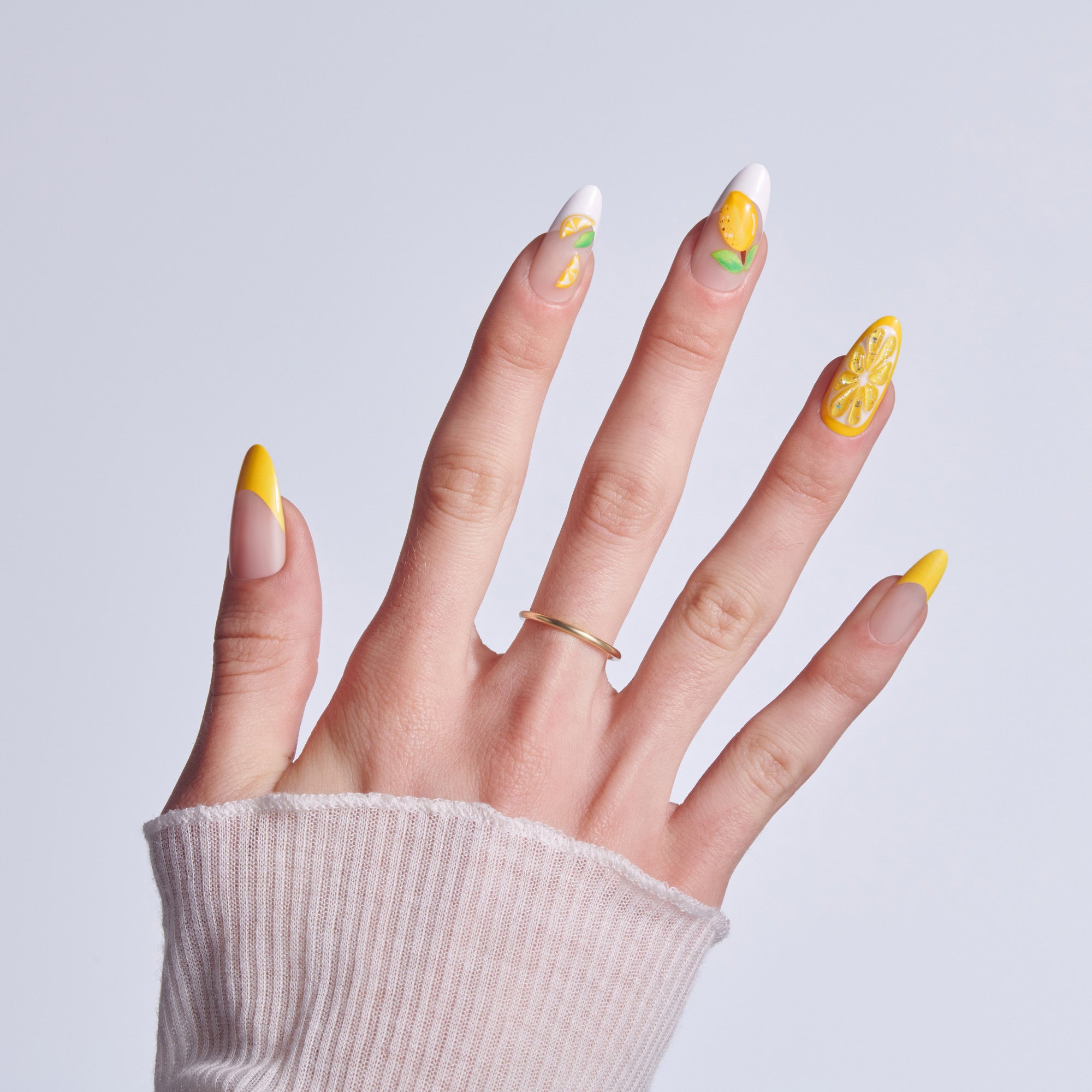 Hand displaying yellow and white lemon-themed manicure with gold ring against light background