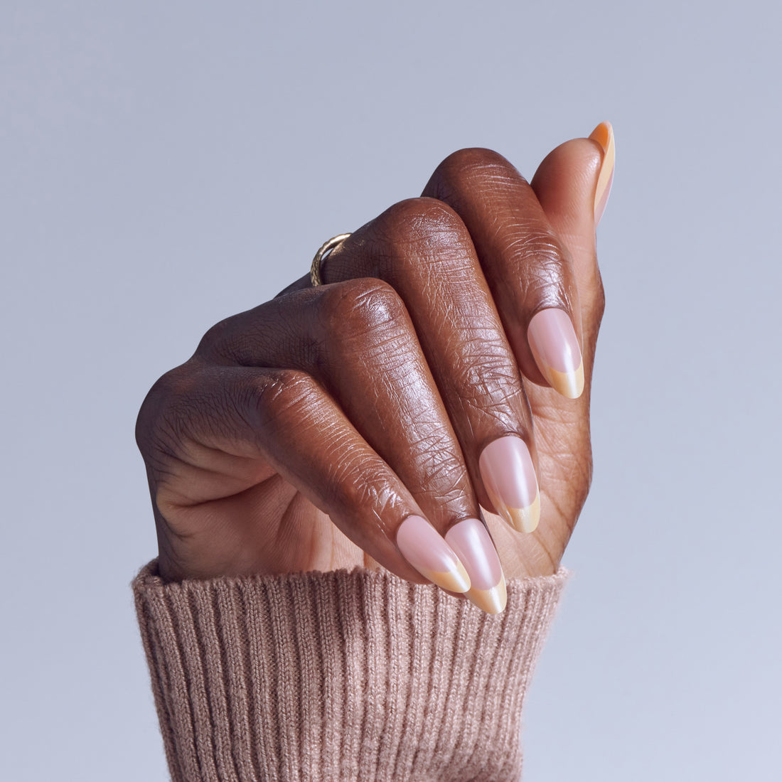 Hand with almond-shaped nails featuring pink and nude ombre manicure against light background.