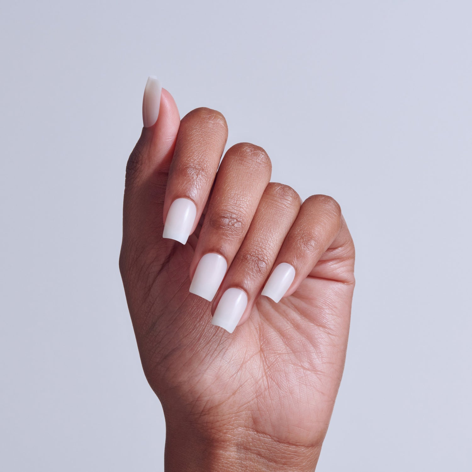 Hand displaying white acrylic nails with square tips against neutral background.