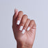 Hand displaying white acrylic nails with square tips against neutral background.
