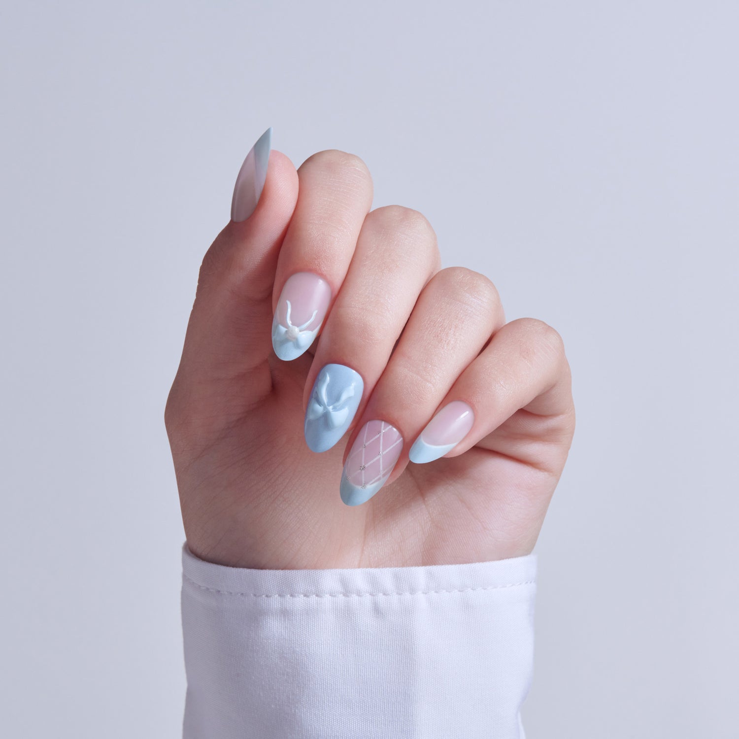 Manicured hand displaying blue, pink, and white nail art with geometric patterns and almond shapes.