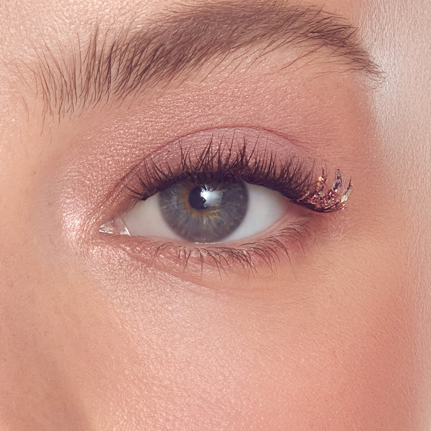 Close-up of eye with gray iris, dark lashes, and rose gold glitter eyeliner.