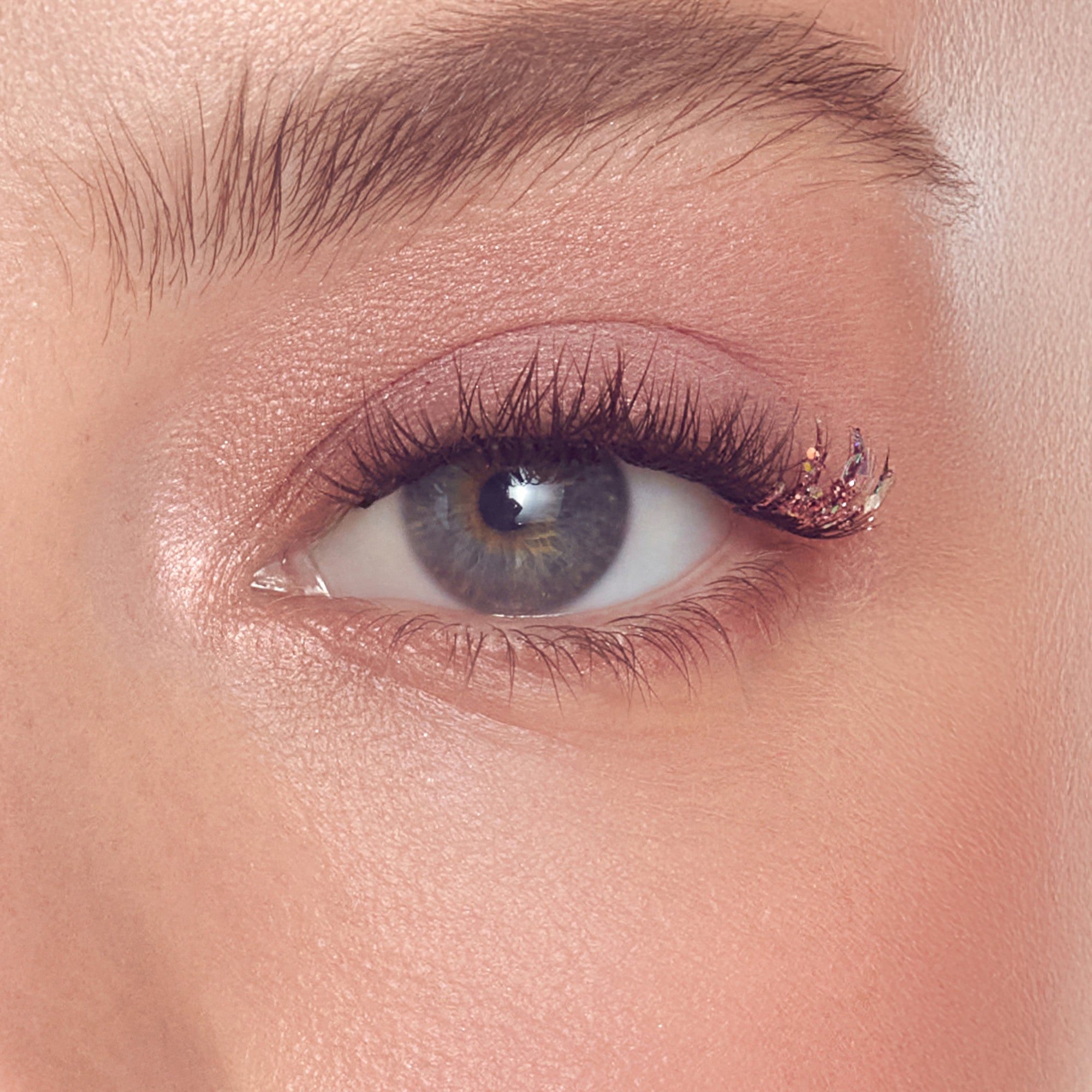 Close-up of eye with gray iris, dark lashes, and rose gold glitter eyeliner.