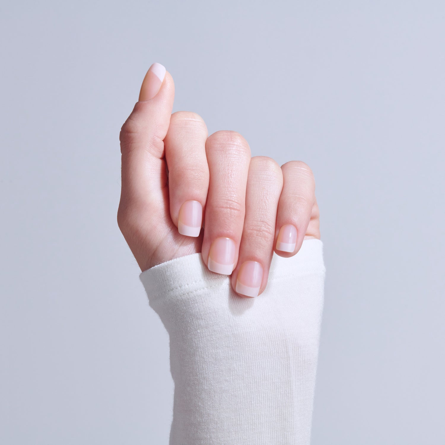 Hand with natural French manicure nails against light gray background