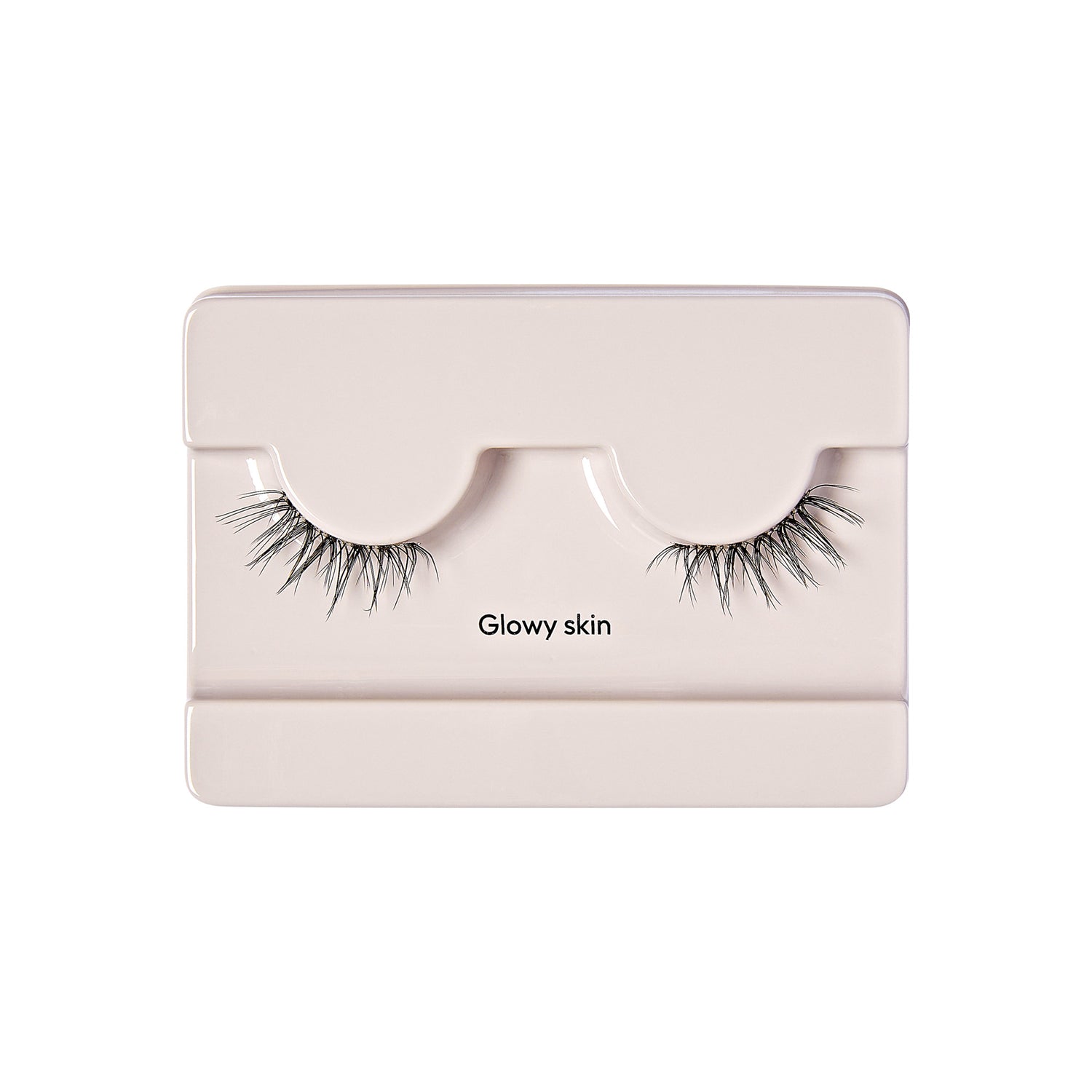 The image shows a pair of false eyelashes in a light-colored plastic packaging. The packaging is designed to hold the eyelashes securely, with two curved indentations where the lashes are placed. The false eyelashes are long and voluminous, with a natural-looking gradient from shorter to longer strands. The text "Glowy skin" is printed on the packaging, positioned between the two sets of eyelashes. The overall presentation is clean and minimalistic.