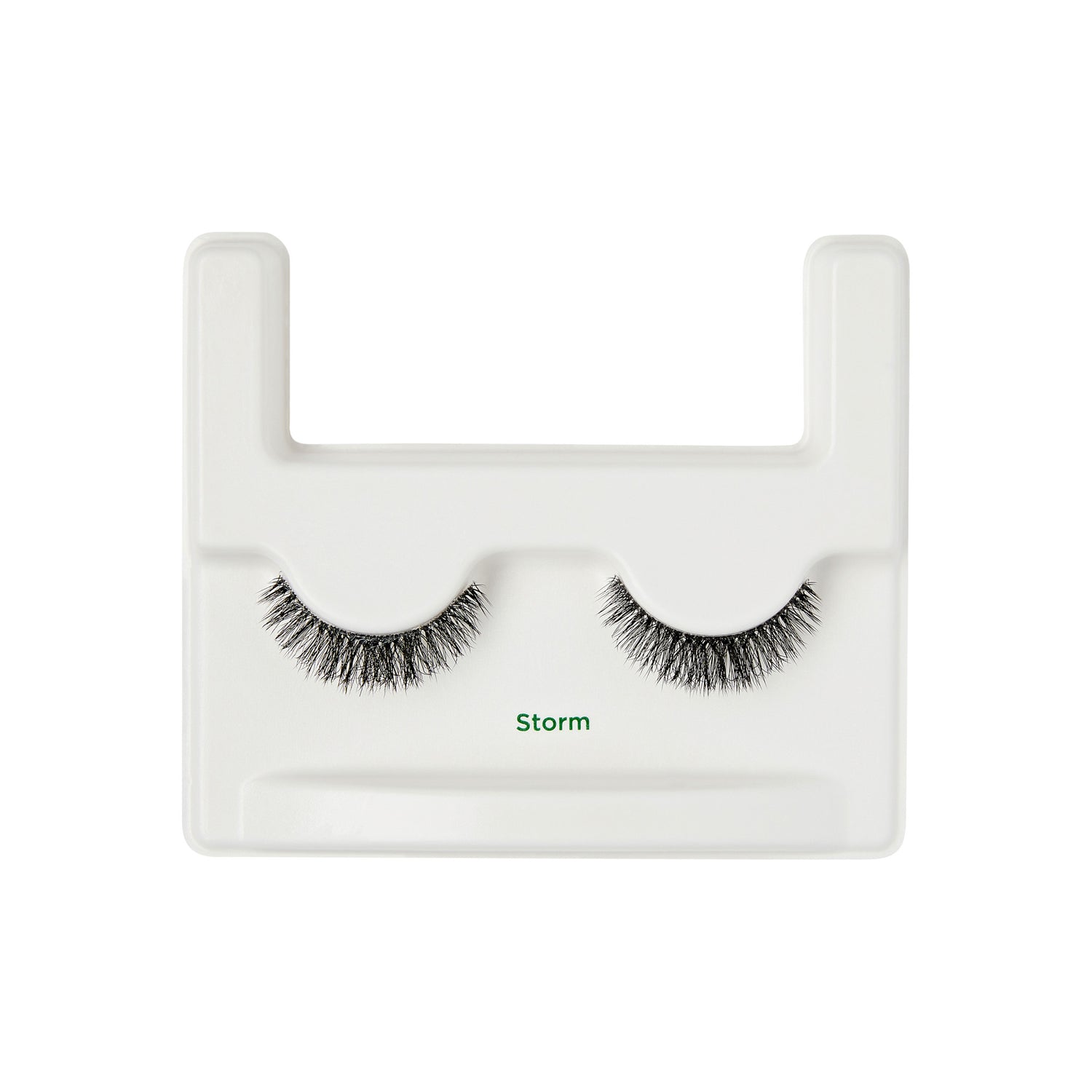 The image shows a pair of false eyelashes displayed on a white plastic holder. The eyelashes are labeled "Storm" in green text. The holder has a U-shaped design with two protruding sections at the top, which help to keep the eyelashes in place. The eyelashes are dense and have a slightly curved shape, designed to enhance the appearance of the eyes when worn.