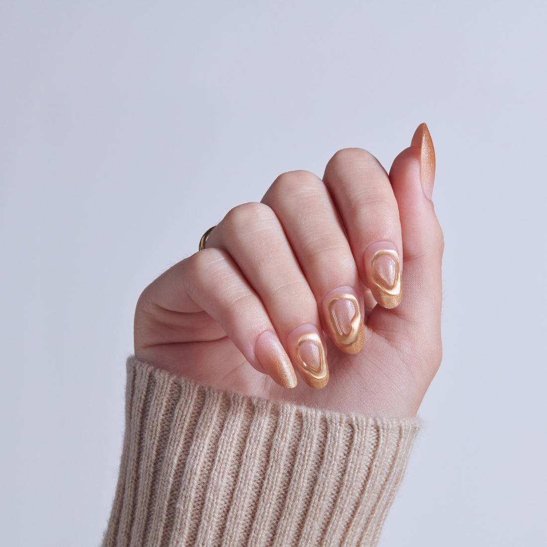 Hand displaying almond-shaped nails with gold and nude gradient nail art design.