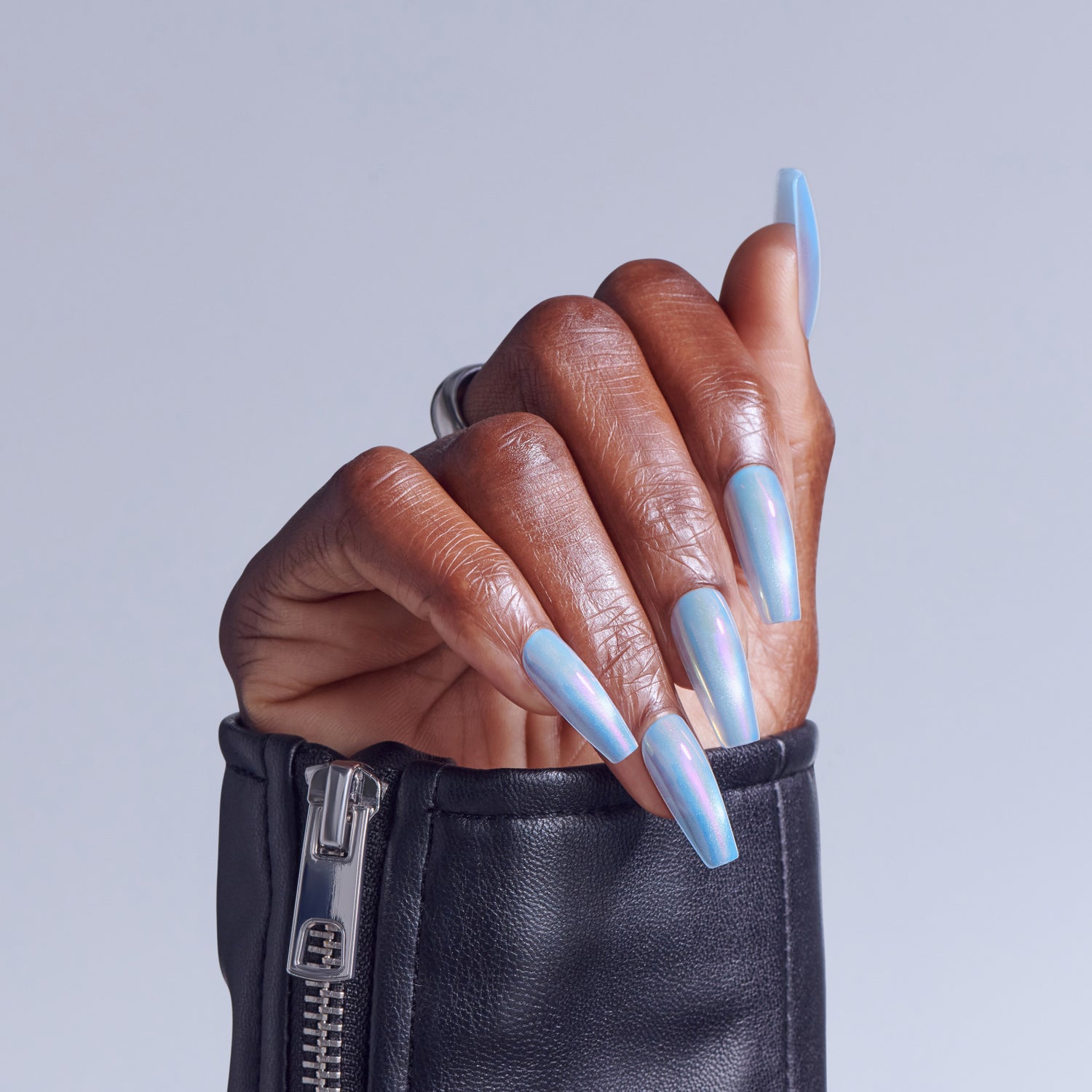 Hand with blue holographic nails emerging from black leather zippered pouch against light blue background.