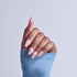 Hand with pink and white checkered nail polish design, wearing blue sleeve against light background.